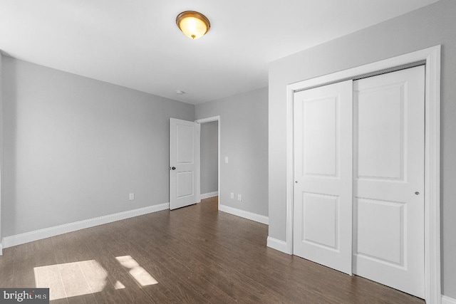 unfurnished bedroom featuring dark wood-style floors, baseboards, and a closet