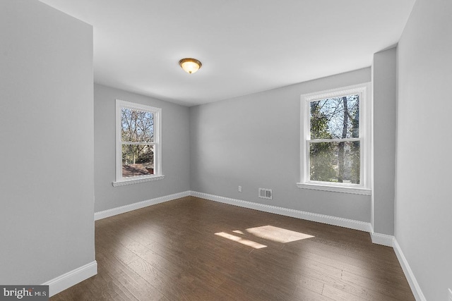 unfurnished room featuring baseboards, visible vents, and dark wood-type flooring