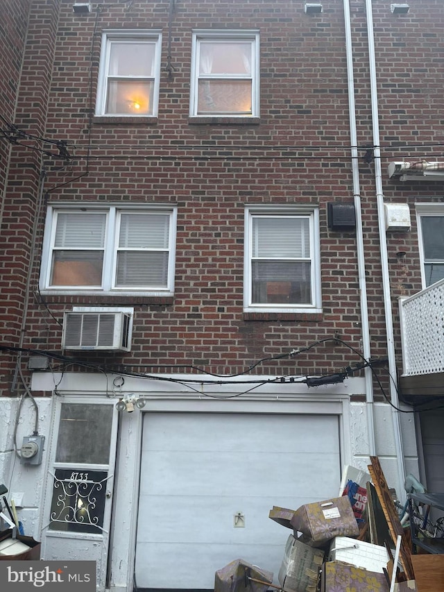 exterior space with an attached garage, brick siding, and a wall mounted air conditioner