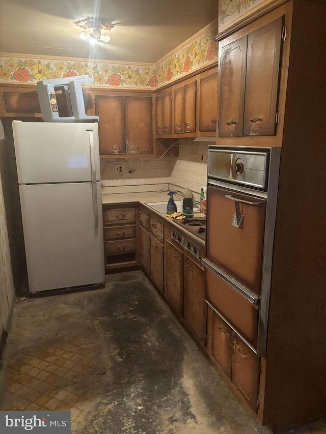 kitchen featuring stainless steel stovetop, light countertops, freestanding refrigerator, brown cabinets, and a warming drawer