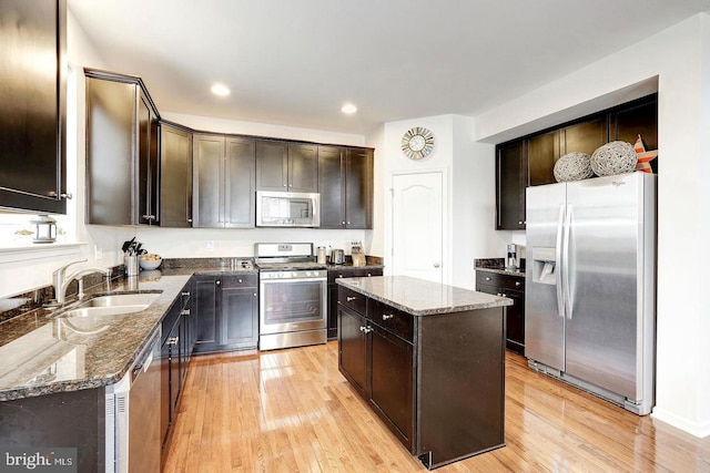 kitchen with dark brown cabinetry, stainless steel appliances, a sink, dark stone counters, and light wood finished floors