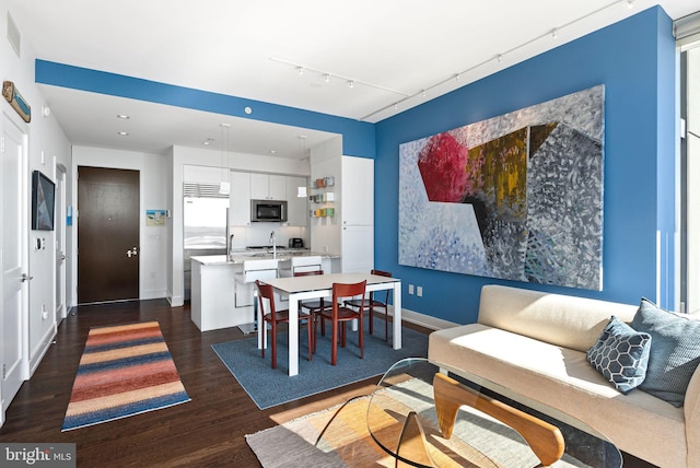 dining space featuring dark wood-style flooring, rail lighting, and baseboards