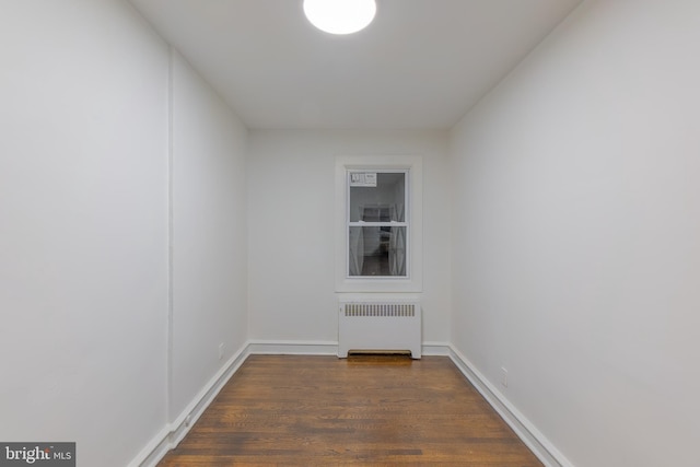 empty room with dark wood-type flooring, radiator heating unit, and baseboards