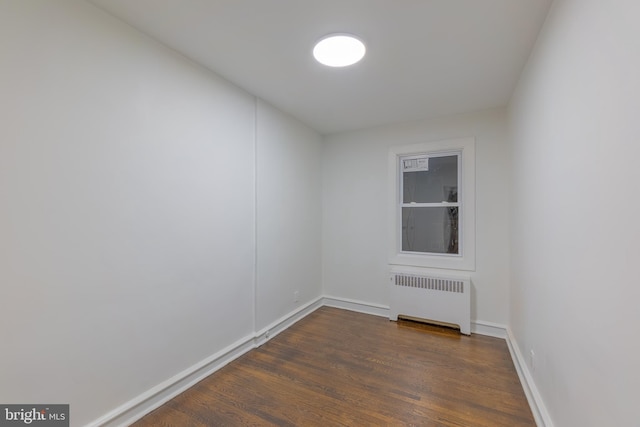 empty room featuring baseboards, dark wood-type flooring, and radiator