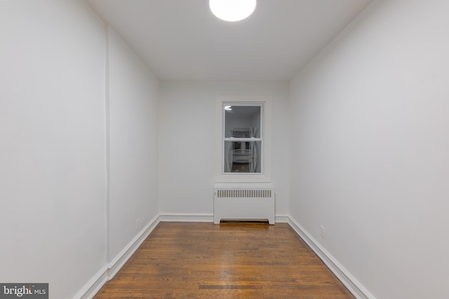 empty room featuring baseboards, radiator heating unit, and wood finished floors