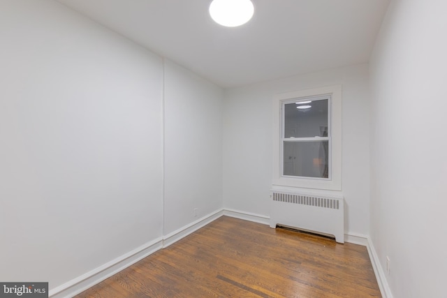 empty room with baseboards, radiator heating unit, and wood finished floors