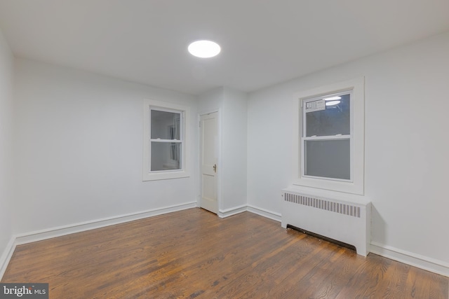 spare room with baseboards, dark wood-style flooring, and radiator