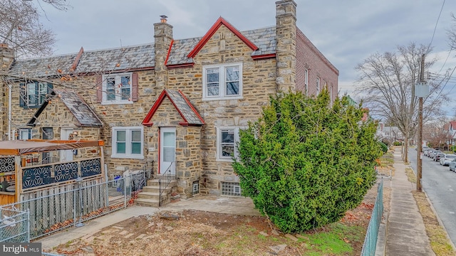 view of front facade with entry steps, stone siding, a high end roof, and fence