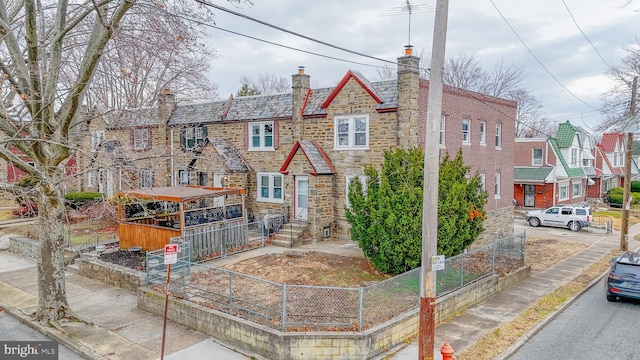 multi unit property featuring a high end roof, stone siding, fence, and a chimney