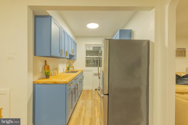 kitchen featuring light wood-style flooring, blue cabinets, butcher block countertops, a sink, and freestanding refrigerator