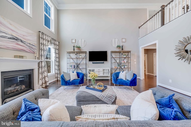 living room with a healthy amount of sunlight, a glass covered fireplace, crown molding, and wood finished floors