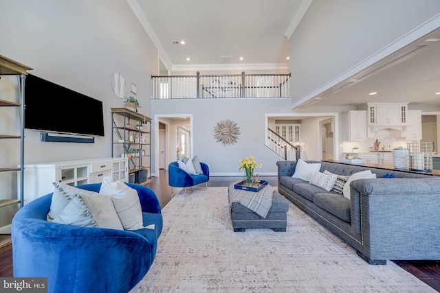 living area with crown molding, stairway, a high ceiling, wood finished floors, and baseboards