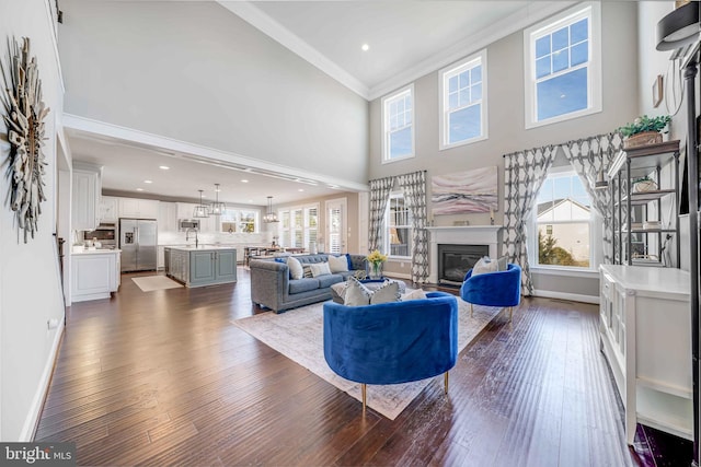 living room featuring dark wood-style floors, a glass covered fireplace, a wealth of natural light, and ornamental molding