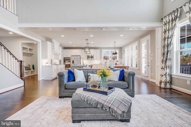 living room with stairs, dark wood finished floors, a towering ceiling, and baseboards