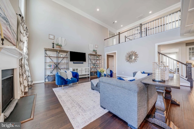 living room featuring a fireplace with raised hearth, a high ceiling, ornamental molding, wood finished floors, and baseboards