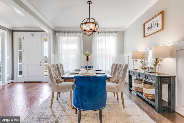 dining room with a chandelier, a decorative wall, a wainscoted wall, wood finished floors, and crown molding