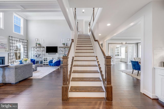 staircase with a glass covered fireplace, hardwood / wood-style flooring, beamed ceiling, a high ceiling, and recessed lighting