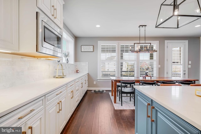 kitchen featuring white cabinetry, light countertops, backsplash, stainless steel microwave, and dark wood finished floors