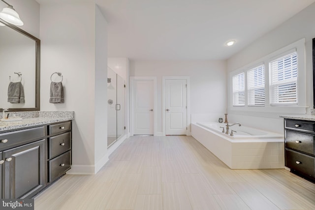 full bathroom featuring a stall shower, baseboards, a garden tub, and vanity