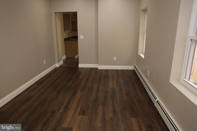 unfurnished room featuring baseboard heating, a sink, baseboards, and dark wood-style flooring