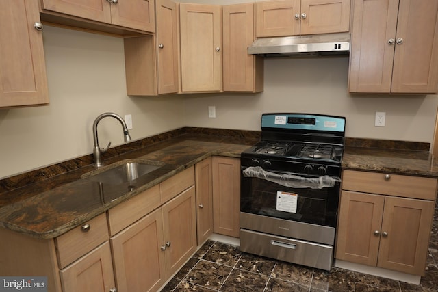 kitchen with a sink, dark stone counters, stainless steel gas stove, and under cabinet range hood