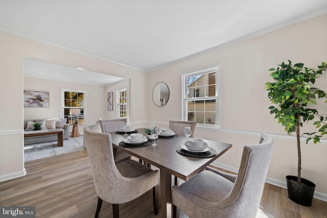 dining space with ornamental molding, light wood finished floors, and baseboards