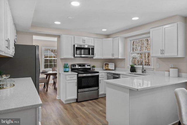 kitchen with recessed lighting, a peninsula, white cabinetry, appliances with stainless steel finishes, and light wood finished floors