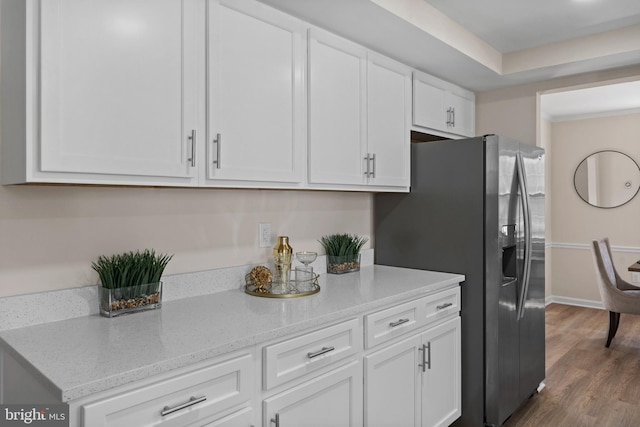 kitchen with light stone counters, stainless steel refrigerator with ice dispenser, white cabinets, wood finished floors, and baseboards