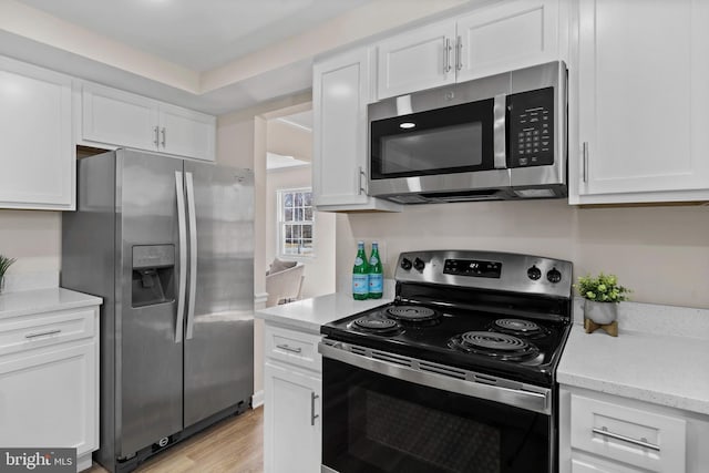 kitchen featuring light wood-style floors, appliances with stainless steel finishes, white cabinets, and light stone counters