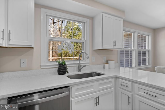 kitchen with white cabinets, a sink, stainless steel dishwasher, and light stone countertops