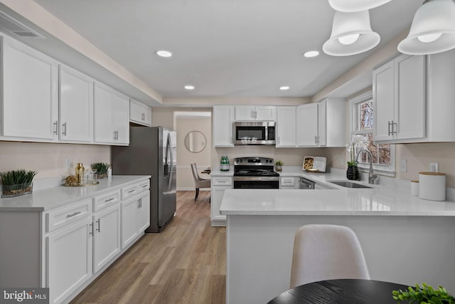 kitchen featuring stainless steel appliances, a peninsula, a sink, and white cabinets