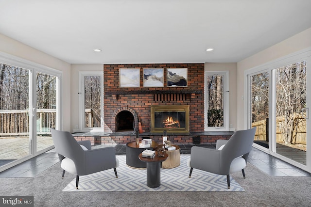 carpeted living area featuring a brick fireplace, stone tile floors, and recessed lighting