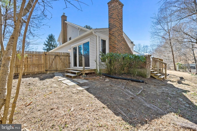 rear view of property featuring entry steps, fence, and a chimney