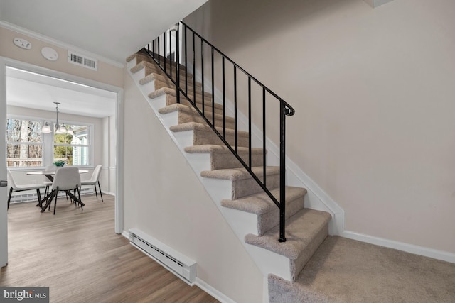 stairs with crown molding, visible vents, baseboard heating, wood finished floors, and baseboards