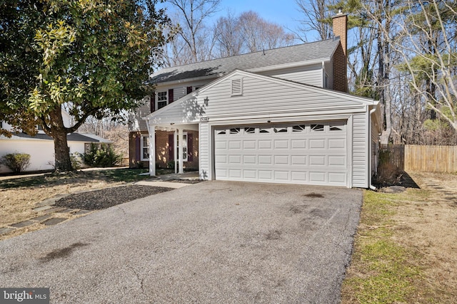 traditional-style house featuring aphalt driveway, a chimney, an attached garage, and fence