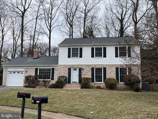 colonial-style house featuring driveway, brick siding, a chimney, an attached garage, and a front yard