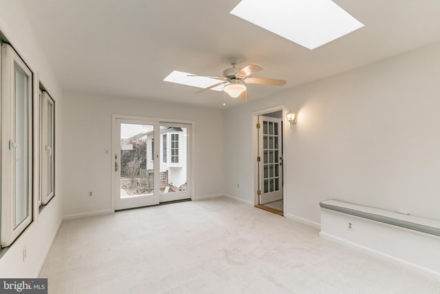 spare room with light carpet, a skylight, a ceiling fan, and baseboards