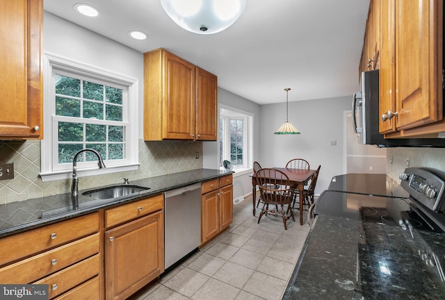 kitchen featuring stainless steel appliances, brown cabinetry, light tile patterned flooring, a sink, and dark stone counters