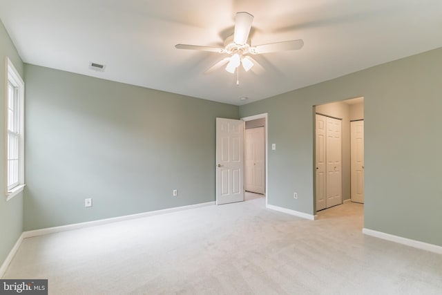 unfurnished bedroom featuring baseboards, visible vents, light colored carpet, ceiling fan, and two closets