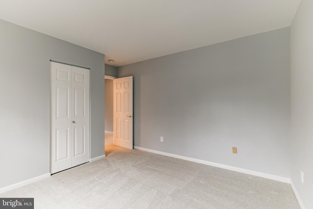 unfurnished bedroom with a closet, light carpet, and baseboards