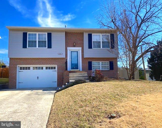 raised ranch featuring a front lawn, brick siding, an attached garage, and driveway