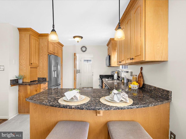 kitchen featuring dark stone countertops, appliances with stainless steel finishes, pendant lighting, and a peninsula