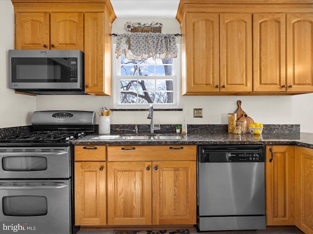 kitchen with dark stone counters, brown cabinetry, appliances with stainless steel finishes, and a sink