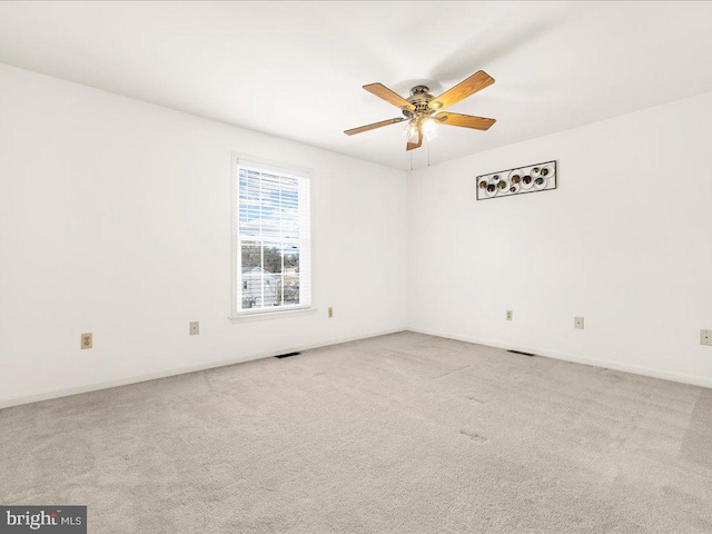 carpeted spare room with visible vents, baseboards, and a ceiling fan