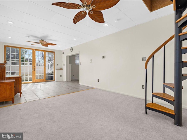 carpeted living area with tile patterned flooring, stairway, baseboards, and ceiling fan