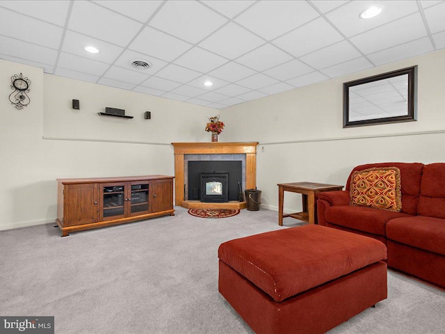 living room featuring baseboards, visible vents, a wood stove, a drop ceiling, and carpet flooring