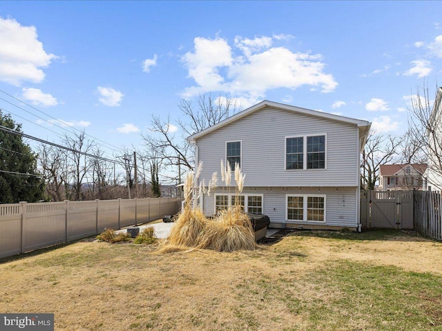 rear view of house with a gate, a fenced backyard, and a yard