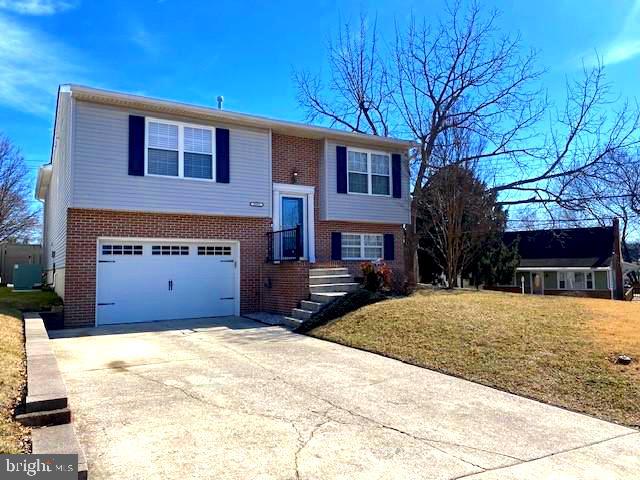 raised ranch with a front lawn, driveway, an attached garage, brick siding, and central AC unit