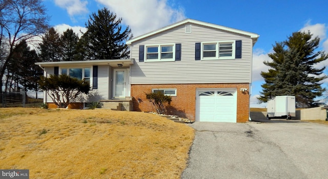 split level home with an attached garage, brick siding, fence, driveway, and a front yard