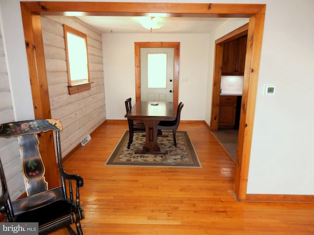 dining area with wood walls, light wood-style flooring, visible vents, and baseboards